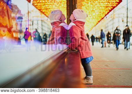 Toddler Girl Looking At Window Glass Of Large Department Store Decorated For Christmas. Child Enjoyi