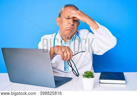 Senior handsome man with gray hair wearing doctor uniform working using computer laptop tired rubbing nose and eyes feeling fatigue and headache. stress and frustration concept. 
