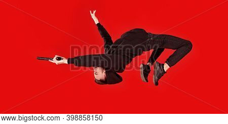 Handsome man in black clothes in motion in flight with a gun. Super agent on a mission. Criminal world, counterterrorism. Studio shot on a red background.