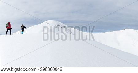 Senior Couple Is Snowshoe Hiking In Alpine Snow Winter Mountains Panorama. Allgau, Bavaria, Germany.