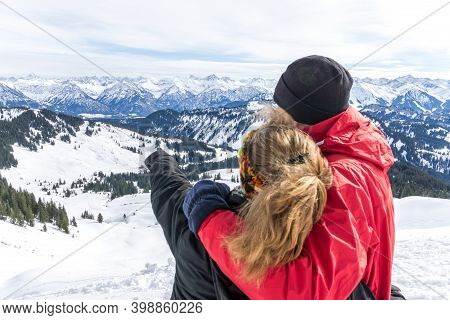 Senior Couple Is Hiking In Alpine Snow Winter Mountains Enjoying Panorama View And Pointing With Fin