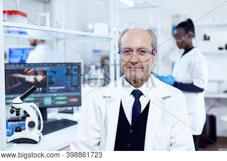 Senior Scientist Sitting At His Workplace During Medical Experiments. Elderly Scientist Wearing Lab 