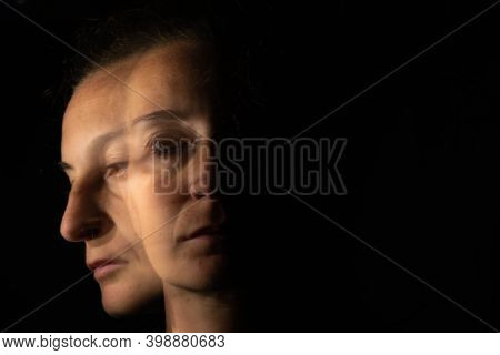 Dark Portrait Of A Serious Woman With Only Half Her Face Lit Up On A Black Background Looking Sad Or