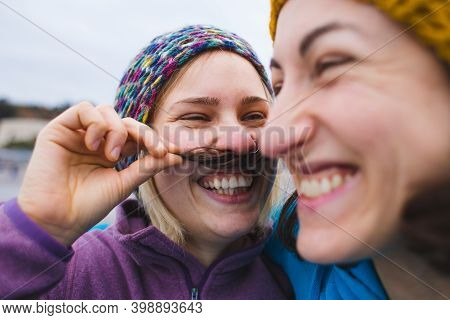 Happy Gay Couple Having Fun Together Outdoor. The Woman Attached An Artificial Mustache. Equality Ri