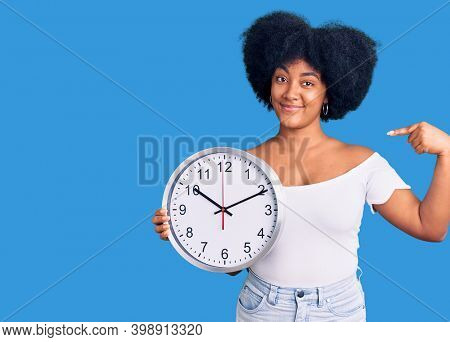 Young african american girl holding big clock pointing finger to one self smiling happy and proud 
