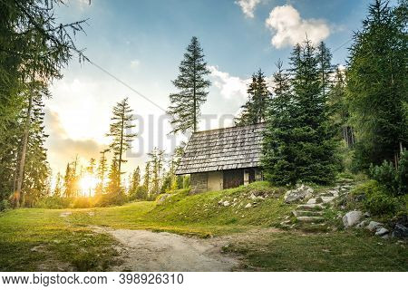 Isolated Cabin In Mountains Surrounded By Deep Forrest, Sunset In Background With Sunrays. Slovakia 