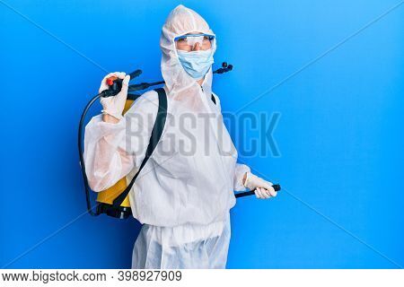 Covid specialist wearing decontamination protective suit and disinfectant spray, decontaminate and sanitize surface, standing over blue background