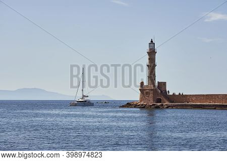 An Ancient Lighthouse In The Port Of Hania In Crete And A Yacht With A Clear And Blue Sky In The Bac