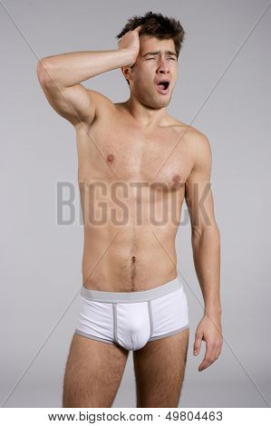 Portrait of young adult sleepy man naked muscular torso in white panties isolated on grey background