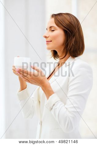 business concept - businesswoman with cup of coffee in office