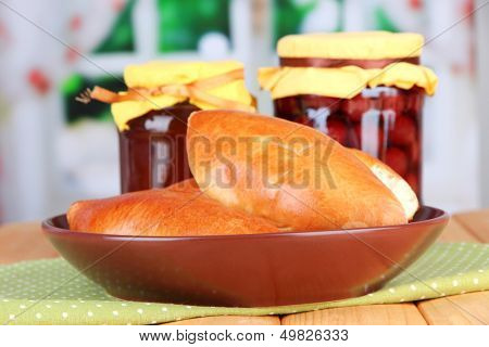 Fresh baked pasties with fruit jam, on wooden table, on bright background