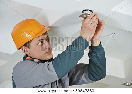 electrician worker in uniform installing or replacing spot light lamp into ceiling