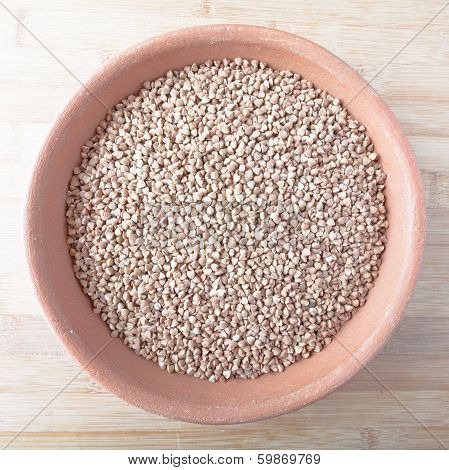 Buckwheat in bowl of clay over wooden background