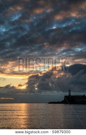 Beautiful Vibrant Sunrise Sky Over Calm Water Ocean With Lighthouse And Harbor Wall