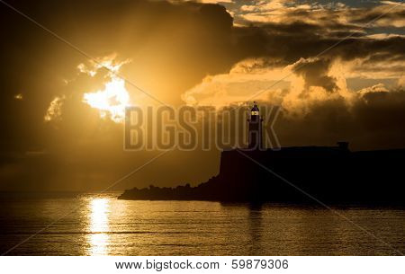 Beautiful Vibrant Sunrise Sky Over Calm Water Ocean With Lighthouse And Harbor Wall