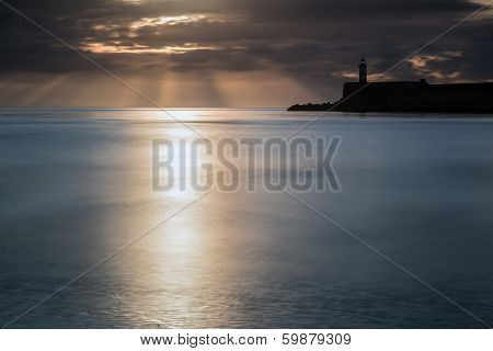 Beautiful Vibrant Sunrise Sky Over Calm Water Ocean With Lighthouse And Harbor Wall