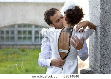 Wedding. Bride with a tattoo kisses the groom. Bride wearing in a sheath dress and hat with veil.