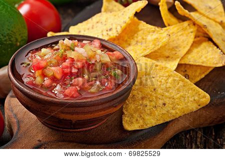 Mexican nacho chips and salsa dip in bowl on wooden background