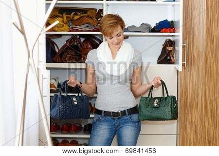 Young woman standing front of wardrobe, unable to decide which bag to take.