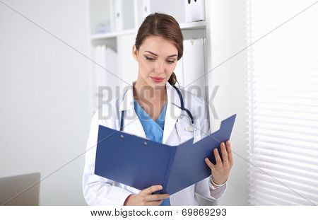Young woman is standing in the near window with folder