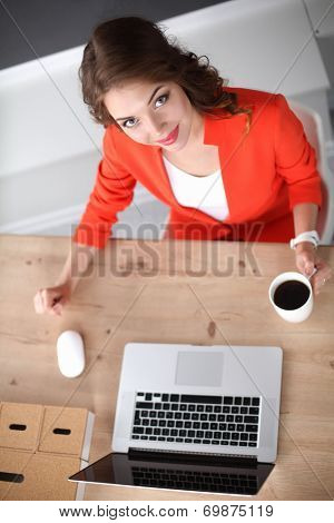 Attractive woman sitting at desk in office, working with laptop ,holding a cup