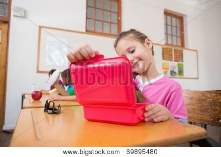 Cute pupil opening lunchbox at desk in classroom at the elementary school