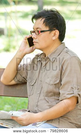 Asiam Man Talking On Phone With Newspaper In Hand.