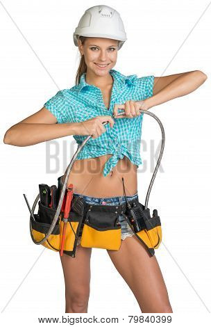 Pretty girl in helmet, shorts, shirt and tool belt with tools connects two flexible hose for plumbin
