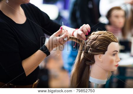 Pretty female hairdresser/haidressing apprentice/student training on an apprentice head