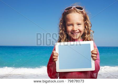Child on the beach with tablet computer. Little happy girl showing screen digital pc