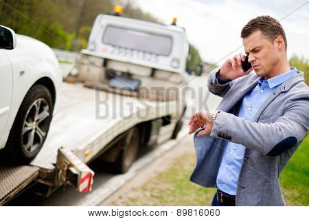 Man calling while tow truck picking up his broken car 