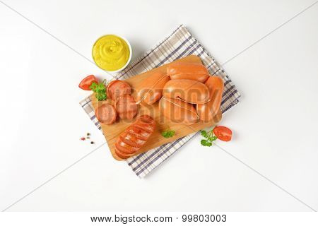 raw and roasted sausages on wooden cutting board