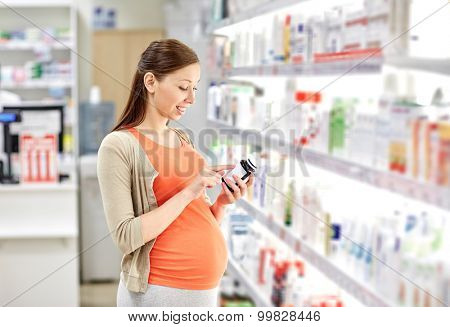 pregnancy, medicine, pharmaceutics, health care and people concept - happy pregnant woman reading label on medication jar at pharmacy
