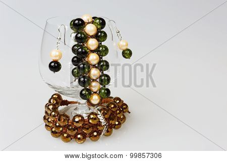 Two Handmade Bracelets With Earrings In A Glass Of Cognac On Isolated White