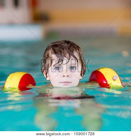 little kid boy with swimmies learning to swim in an indoor pool