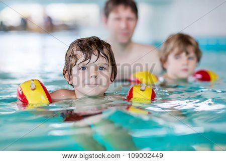 Young dad teaching his two little sons to swim indoors