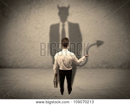 An experienced tricky businessman in suit looking at his devil desguise shadow reflected on the wall concept