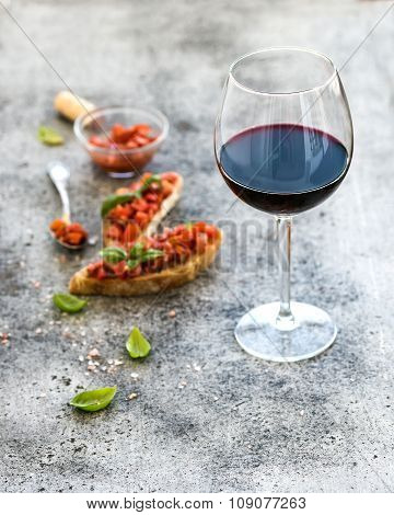 Wine appetizer set. Glass of red wine, brushettas with fresh tomato and basil on over rustic grunge