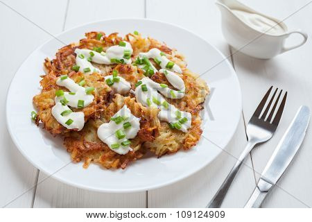 White plate of potato pancakes or latke traditional homemade vegan food with greens and sour cream o
