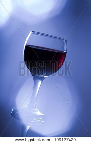 Glass of red wine in cold blue tone with flare.