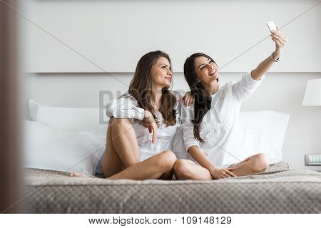 Two Hot Girls Lying  On A Bed Taking A Photo Of Themselves With A Phone
