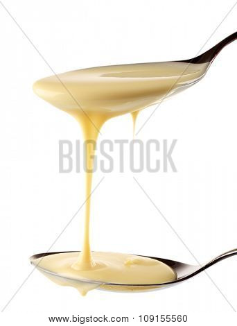 Condensed milk pouring from spoons, isolated on white