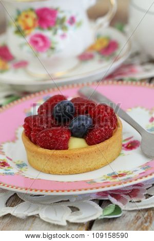 Delicious crunchy tartelette with custard, fresh raspberries and blueberries with cup of tea