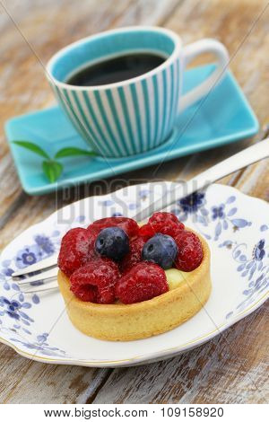 Crunchy tartelette with fresh fruit and cup of coffee on rustic wooden surface
