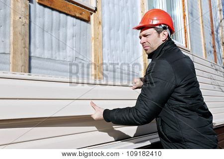A Worker Installs Panels Beige Siding On The Facade Of The House