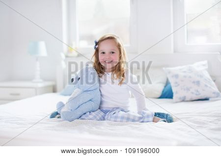 Little Girl Playing With Toy And Reading A Book In Bed