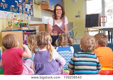 Group Of Pre School Children Listening To Teacher Reading Story