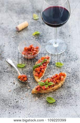 Wine appetizer set. Glass of red wine, brushettas with fresh tomato and basil on over rustic grunge