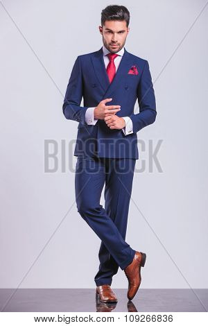 full body picture of handsome man in suit with legs crossed while touching hands