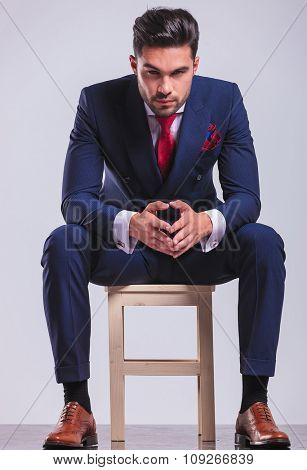 corporate young man sitting in studio with palms touching while posing